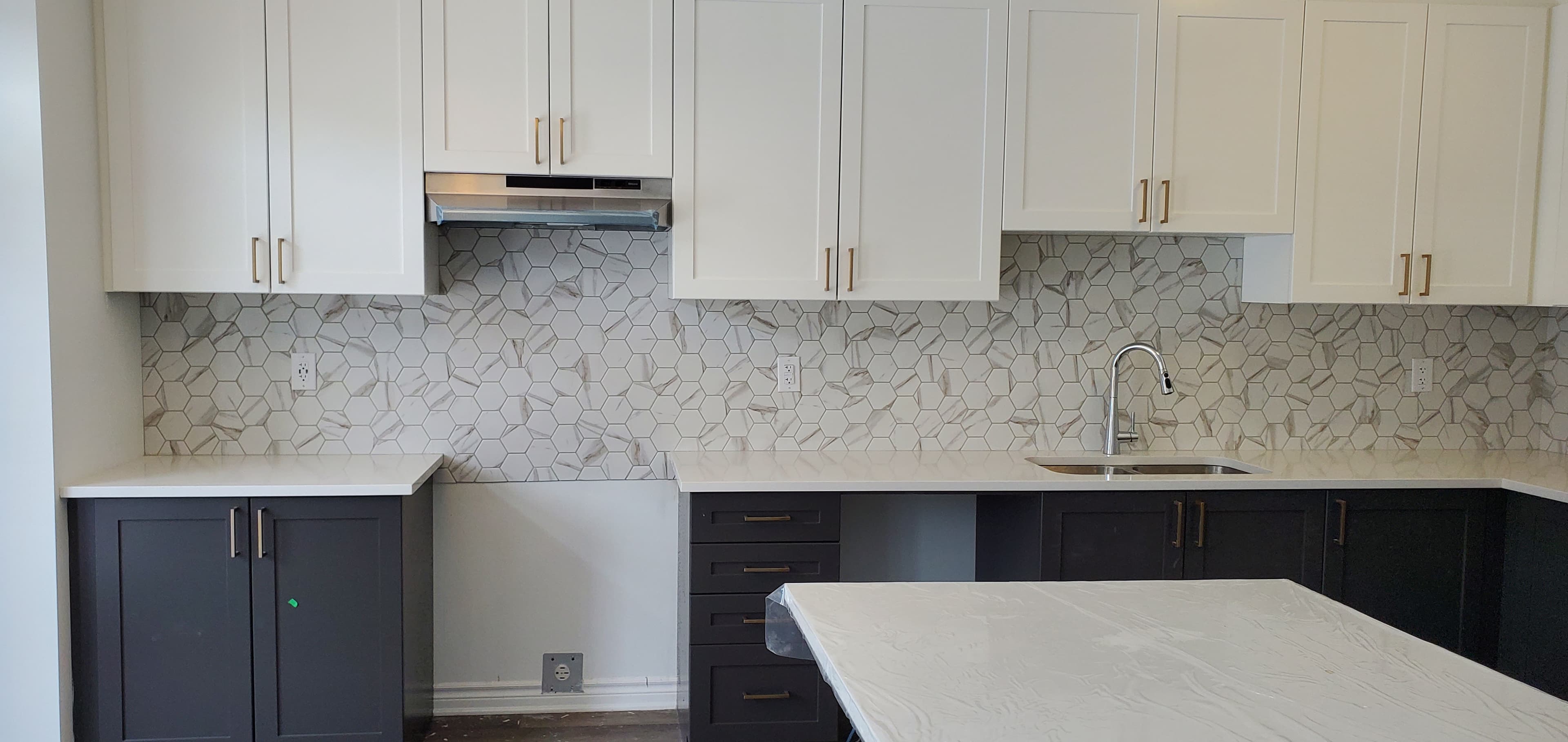 Modern kitchen with white and dark cabinets, gold hardware, and marble hexagonal tile backsplash.