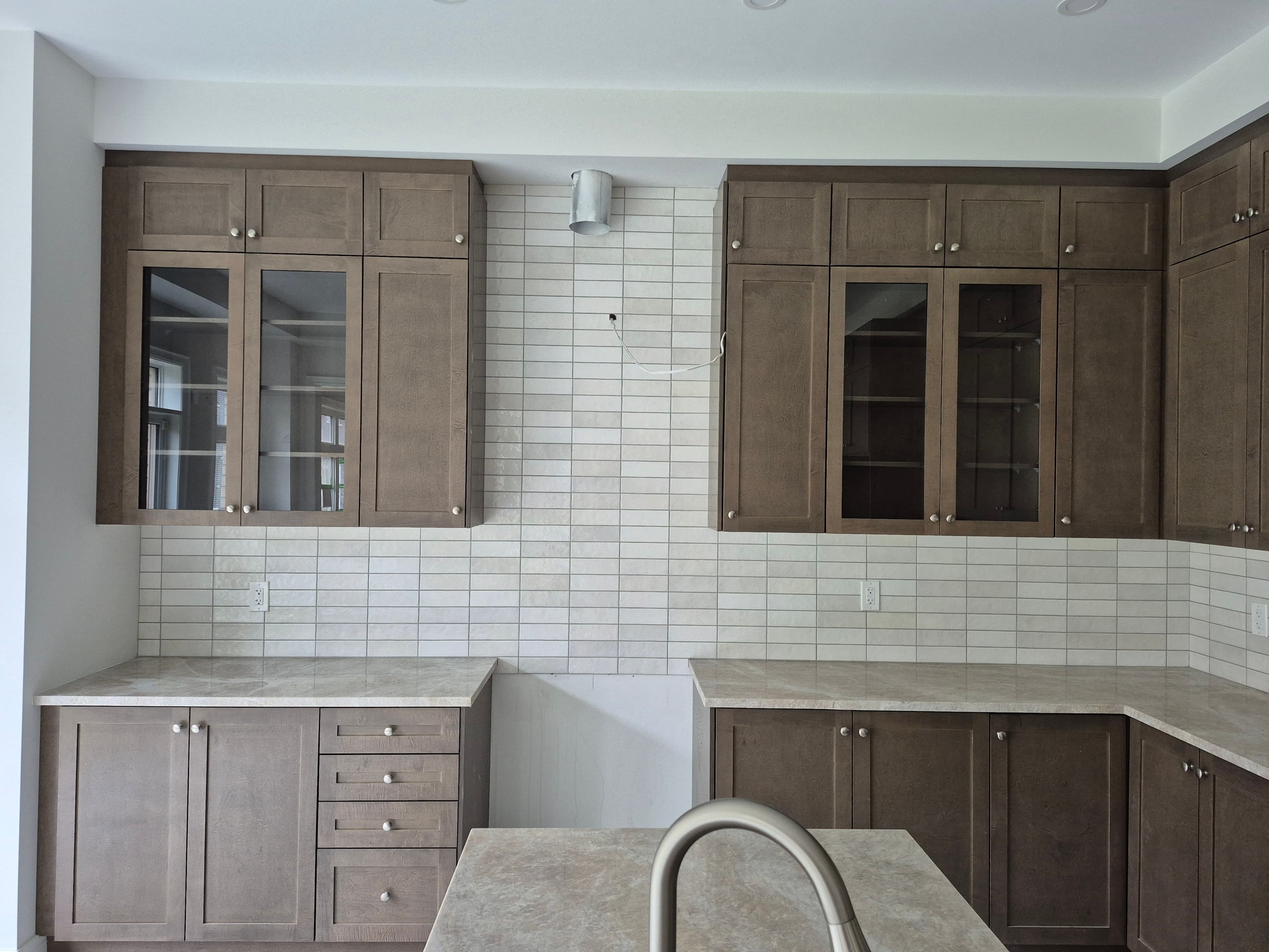 Modern kitchen with brown wood cabinets, white subway tile backsplash, and light stone countertops.