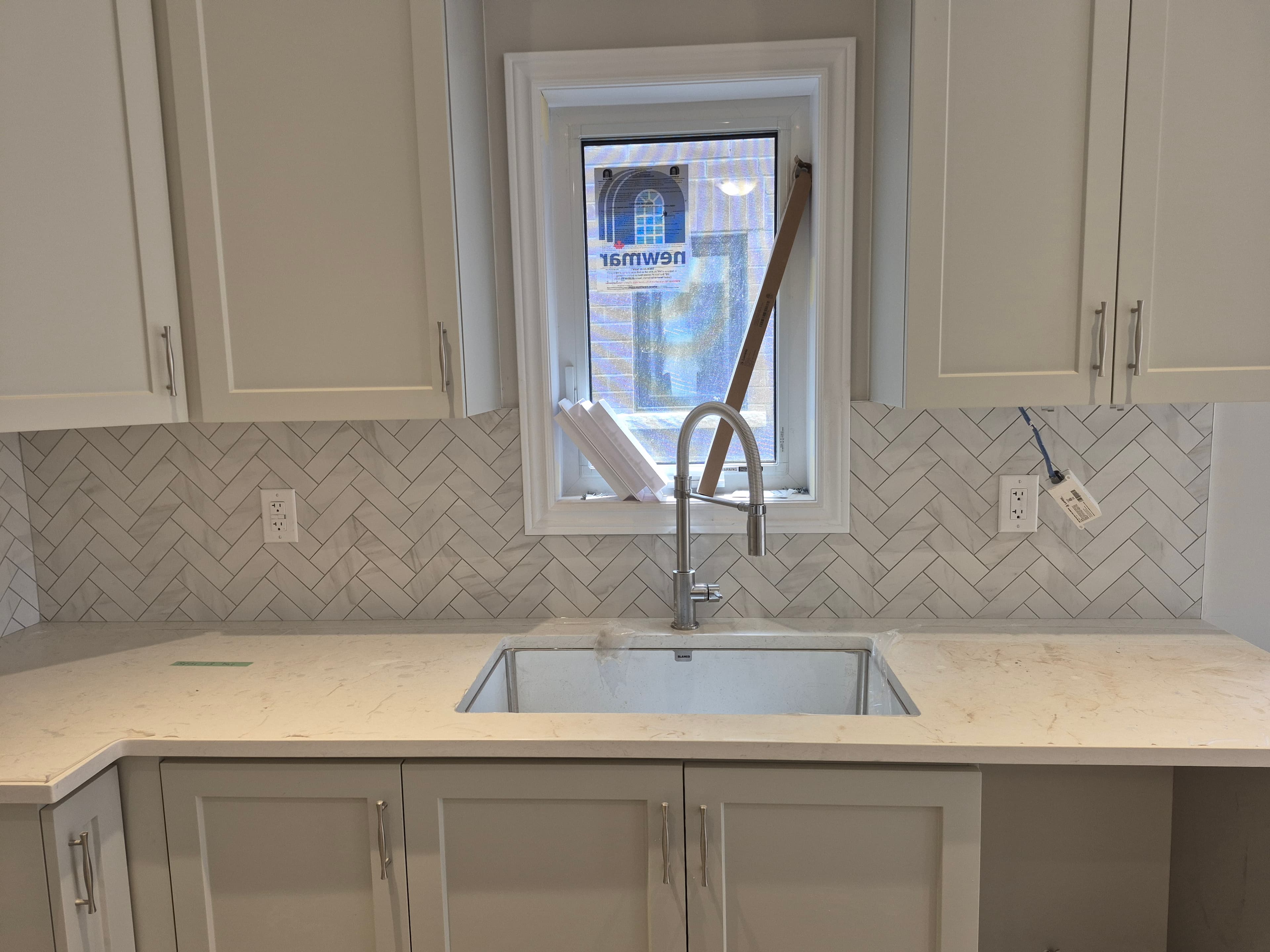 Modern kitchen with white shaker cabinets, herringbone tile backsplash, and stainless steel undermount sink.