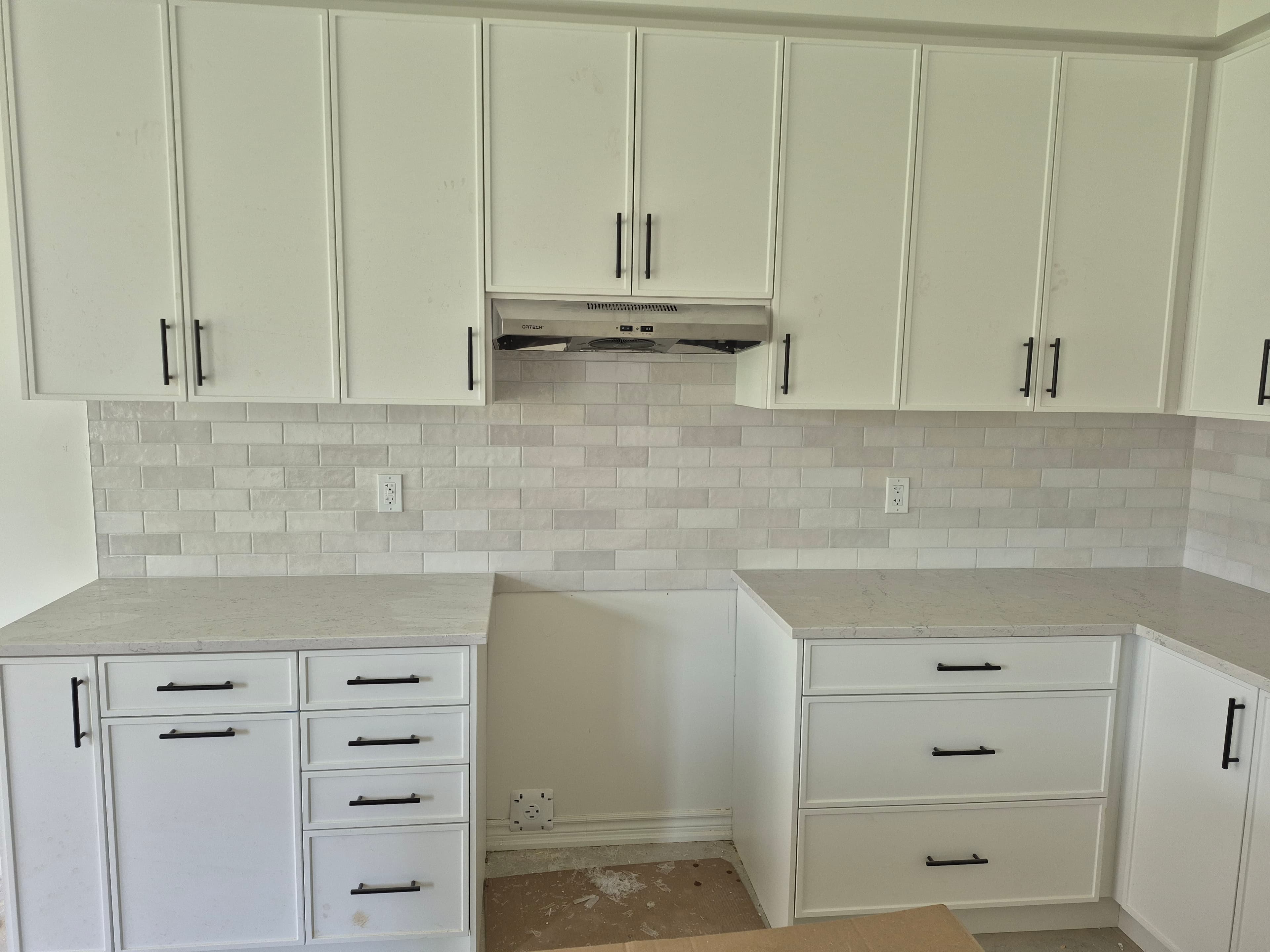 Modern white kitchen cabinets with black hardware, subway tile backsplash, and light marble countertops.